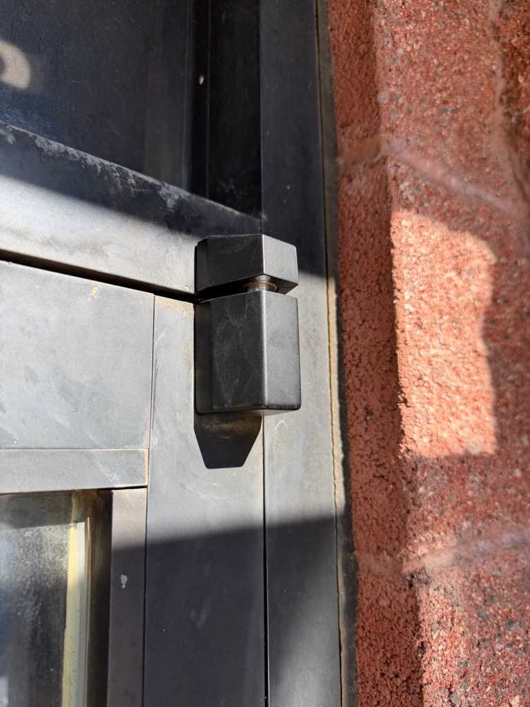 Close-up of a black storefront door upper pivot.